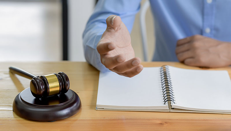 La main d'un homme tendu vers l'avant portant une chemise bleu. Il y a également un marteau de juriste à coté