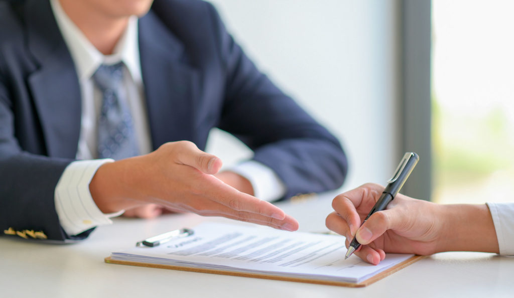 un homme assis en veste bleu explique et fait signer un contrat à son client en face de lui